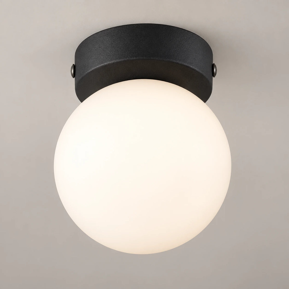 Plafonnier boule en verre blanc allumé sous son embase ronde en métal noir mat