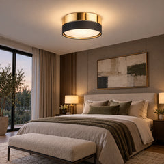 Plafonnier rond noir et doré allumé au plafond d'une chambre, au-dessus du lit